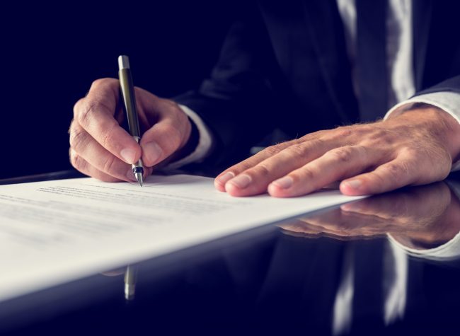 Signing legal document Retro image of lawyer signing important legal document on black desk. Over black background.